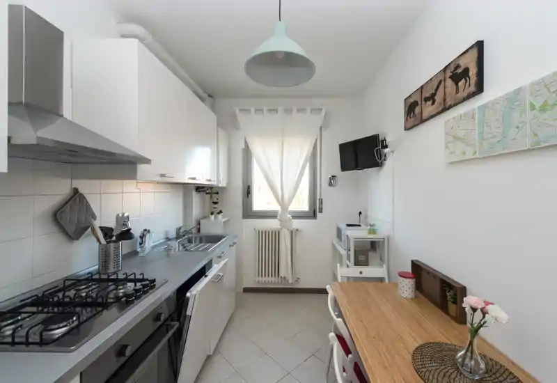 Bright, compact kitchen with modern appliances, a gas stove, stainless sink and a small wooden dining surface — ideal for a cozy apartment.