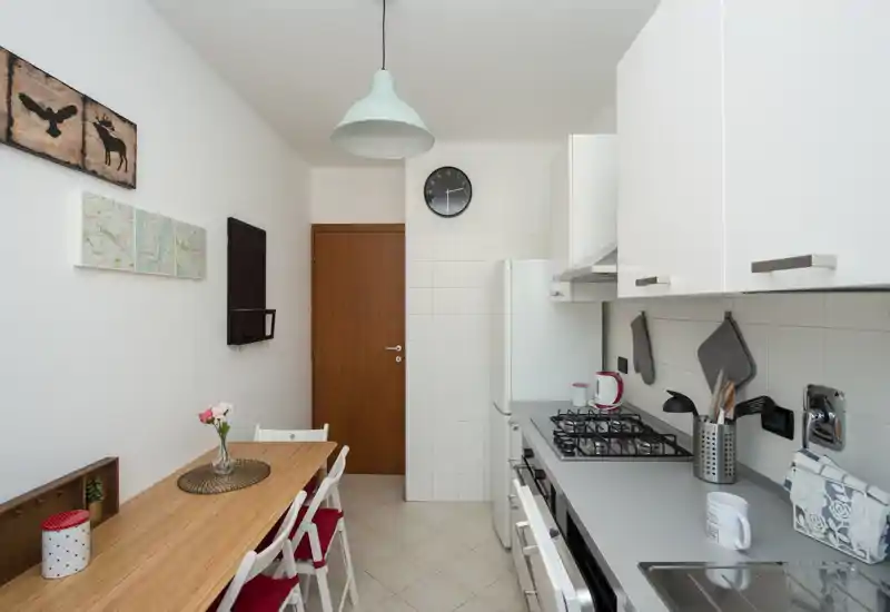 Bright, compact kitchen with a gas hob, stainless sink and a wooden dining table with chairs — neat, well organized and welcoming for short stays.