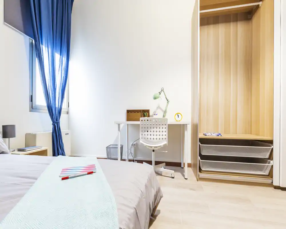 Bright, modern bedroom with a neatly made bed, study desk and open wardrobe. Natural light and clean styling create an airy, comfortable atmosphere ideal for rentals.