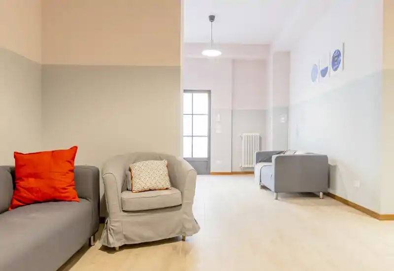 Espacio de salón moderno y luminoso con butacas y sofá cómodos, paredes en tonos pastel y suelo de madera — perfecto para relajarse.