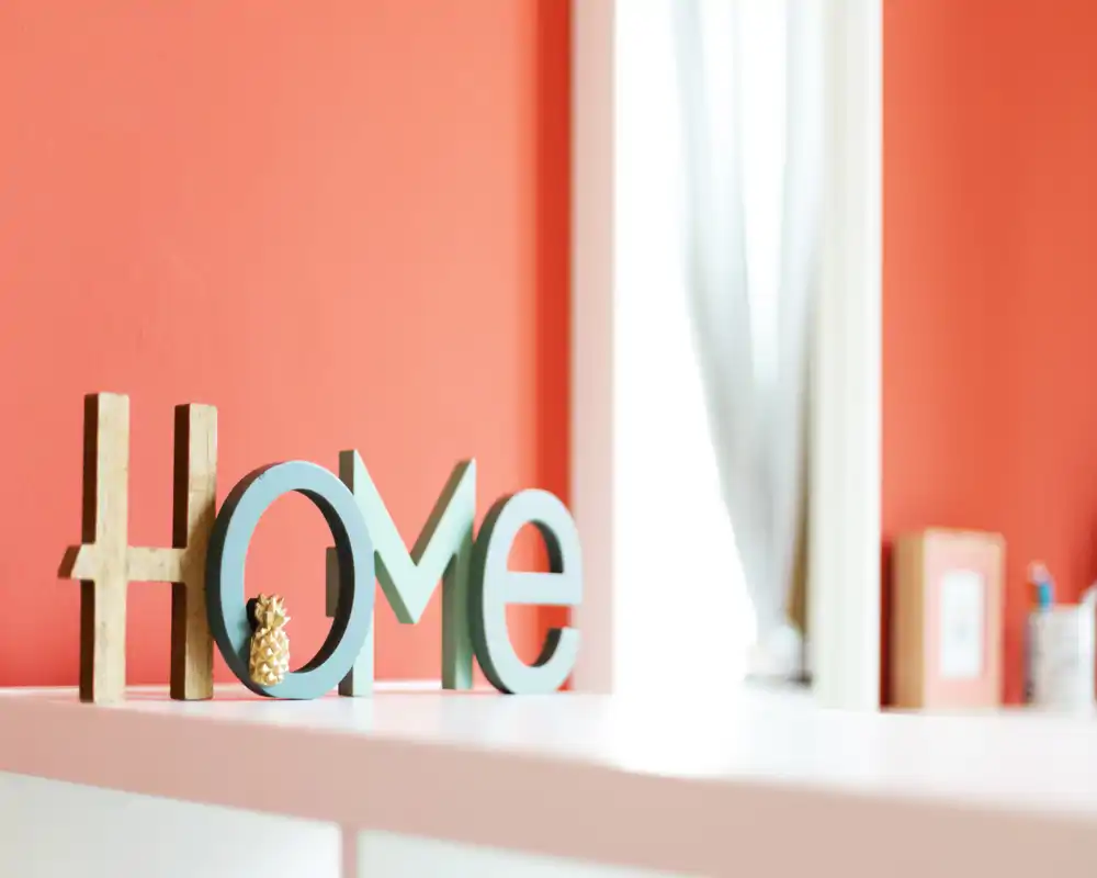 Bright, stylish living area detail featuring decorative "HOME" letters on a white surface against a warm coral wall and soft natural light.