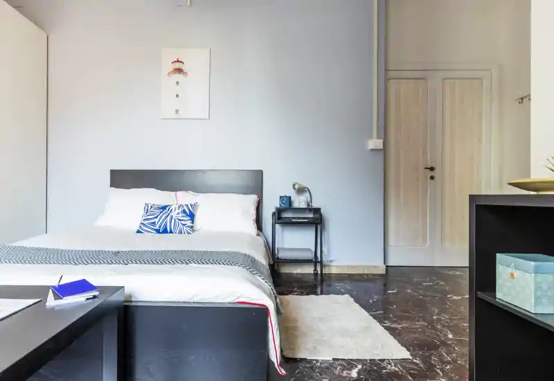 Bright, modern bedroom with a full bed, decorative throw pillow and a bedside table. Clean lines, neutral wall tones and natural light create a calm, welcoming atmosphere ideal for listings.