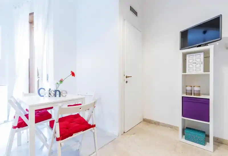 Bright, modern dining corner with a small white table, folding chairs with red cushions and a decorative flower—ideal for cozy breakfasts.