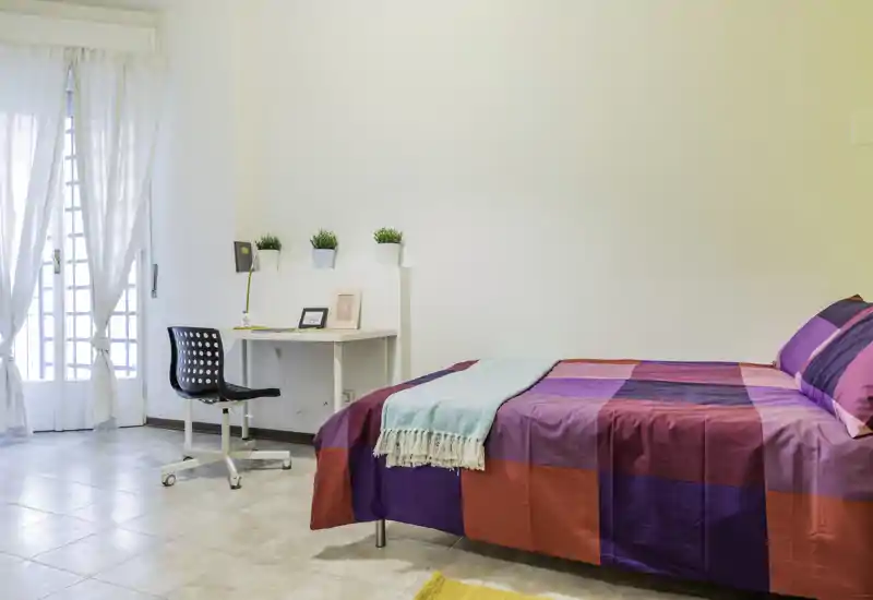 Bright, well-styled bedroom with a colorful double bed, a small desk and natural light from a balcony door. The room feels fresh and inviting, ideal for rental listings highlighting comfort and workspace.