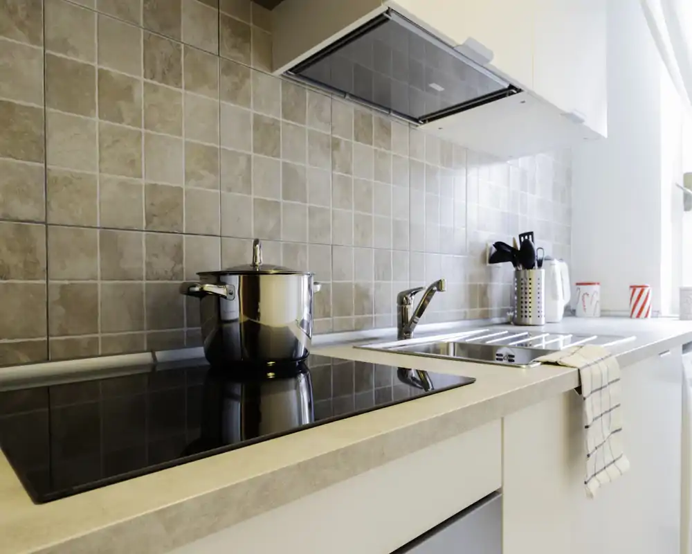 Cucina moderna compatta con piano a induzione, pentola in acciaio, lavello integrato e luce naturale intensa — spazio pulito e funzionale, ideale per affitti brevi.
