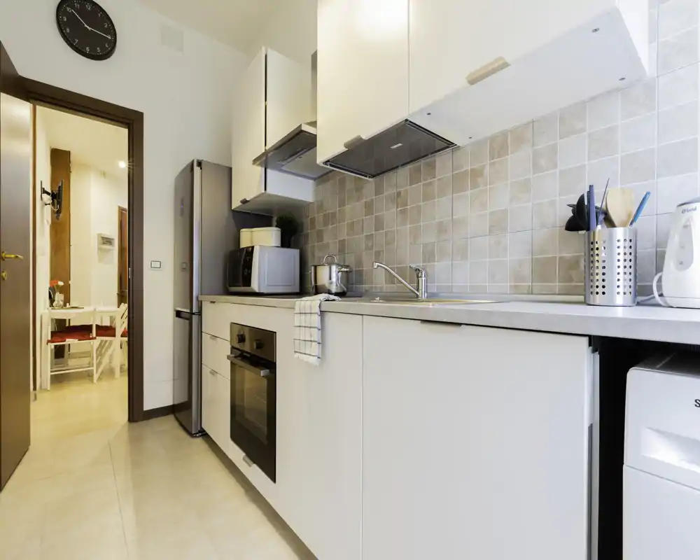 Cucina moderna e compatta con paraschizzi piastrellato, forno integrato, frigorifero e lavello; luminosa, ordinata e pronta all'uso.
