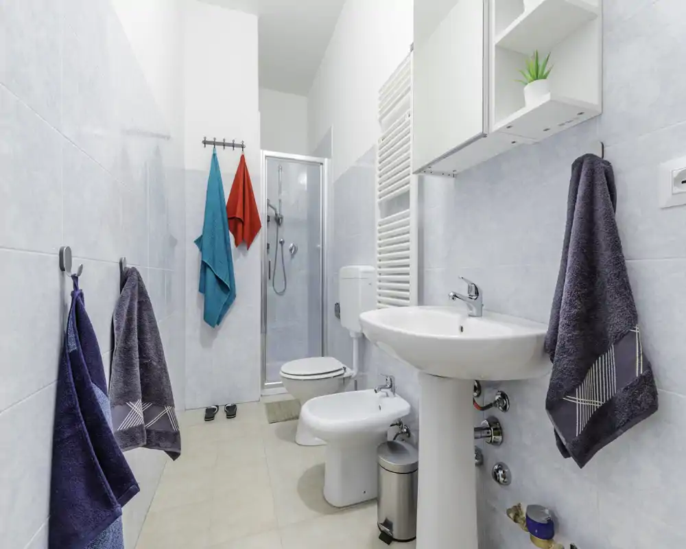 Bagno moderno e luminoso con lavabo, bidet, WC e box doccia; piastrelle azzurro chiaro e diversi asciugamani che danno un aspetto fresco e pulito.