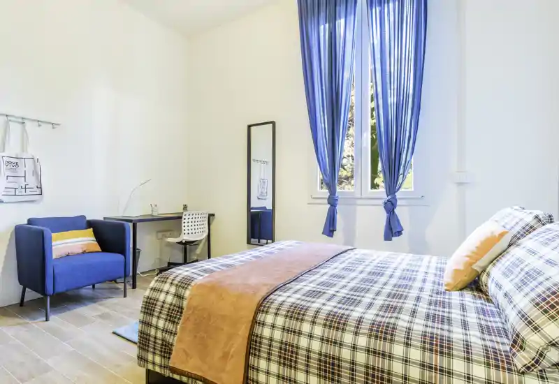 Dormitorio luminoso y bien decorado con cama doble estampada, textiles acogedores y luz natural por la ventana — perfecto para alquileres.