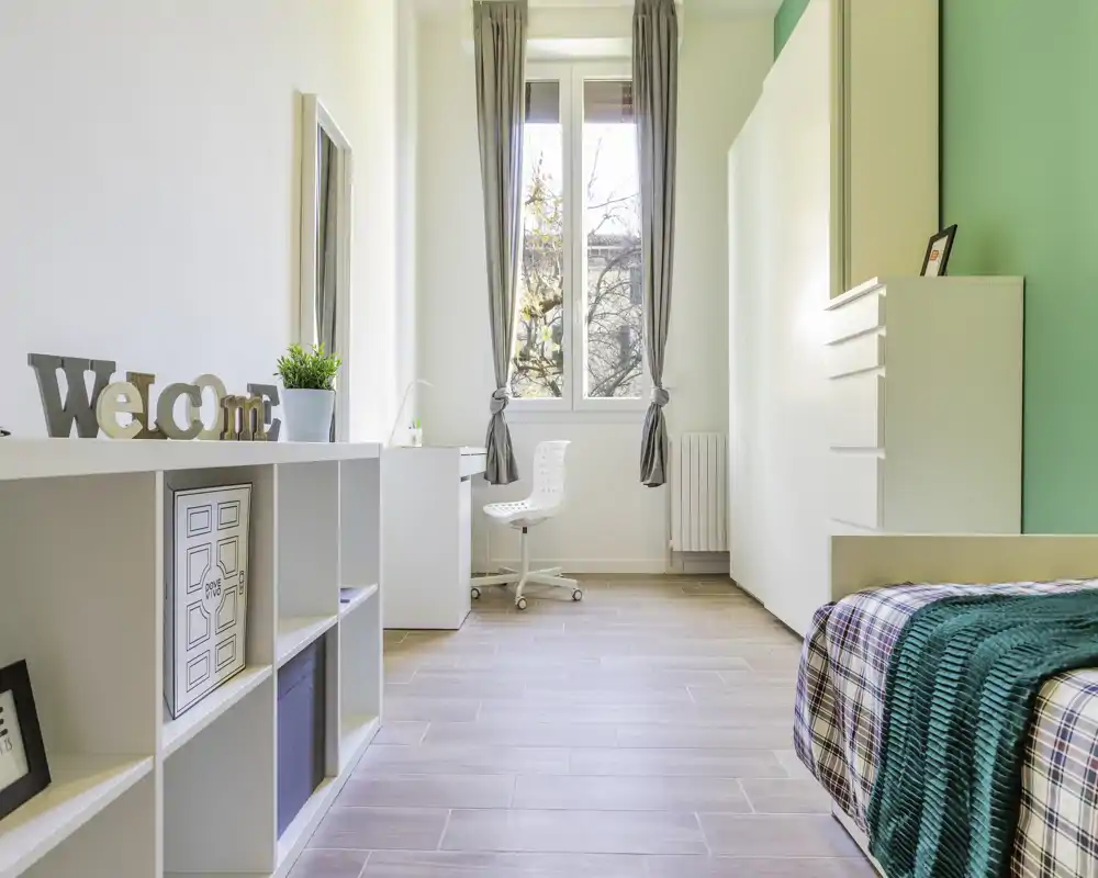 Bright, modern bedroom with a neatly made single bed, natural light from a central window, and clean minimalist furnishings ideal for a rental listing.