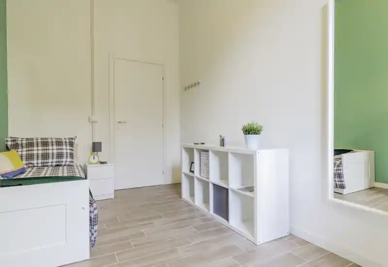 Bright, modern single bedroom with a white bed, bedside table and shelving unit; clean lines and green accent wall give a fresh, minimalist feel.