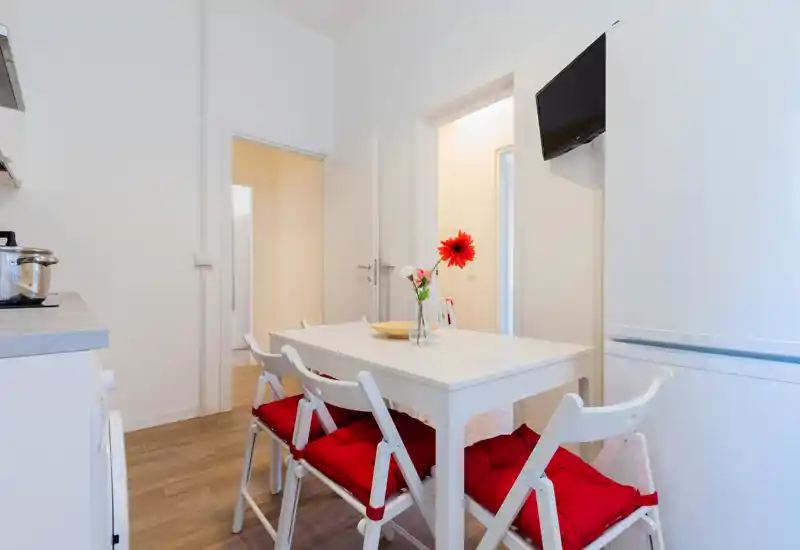 Bright compact kitchen with a small dining table set for four, red cushions and a cheerful flower centerpiece create a welcoming atmosphere.