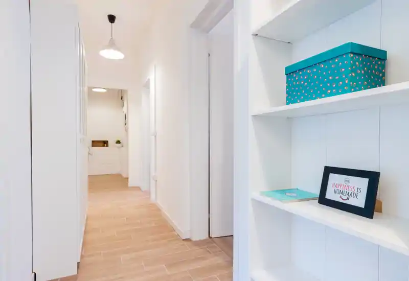 Bright, minimal hallway with white walls, built-in shelving and wood-effect tile flooring — a clean, welcoming entrance area.