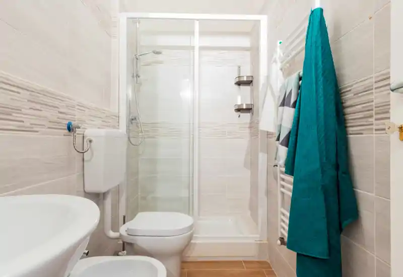 Bright, modern bathroom with a glass shower enclosure, wall-mounted radiator with towels, toilet and sink—clean, well-lit space ideal for rental photos.