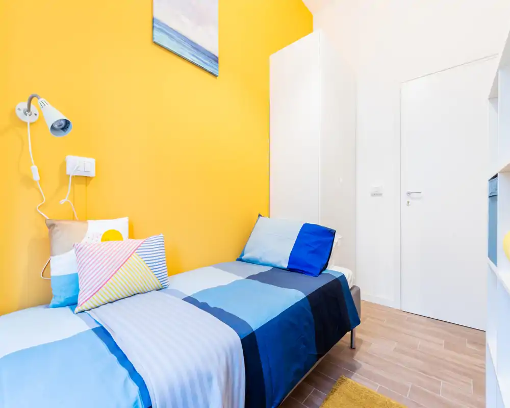 Petite chambre lumineuse avec lit simple bien fait, textiles colorés et armoire blanche — style frais et joyeux, parfait pour une annonce locative.