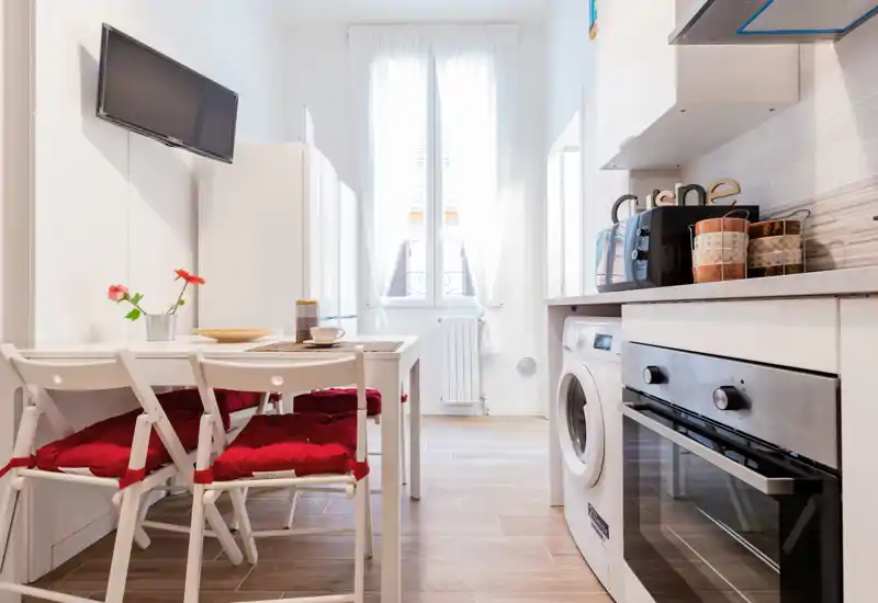 Bright, compact kitchen with modern appliances, a small dining table and cozy red seat cushions — ideal for a city apartment.