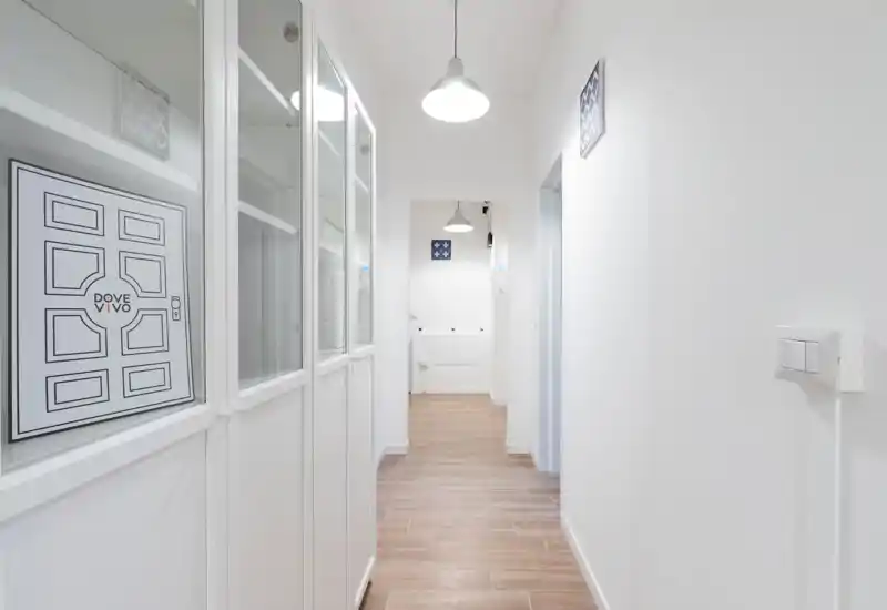 Bright, modern entrance hallway with white walls, pendant lighting and wood-effect floor tiles, offering a clean welcoming approach to the apartment.