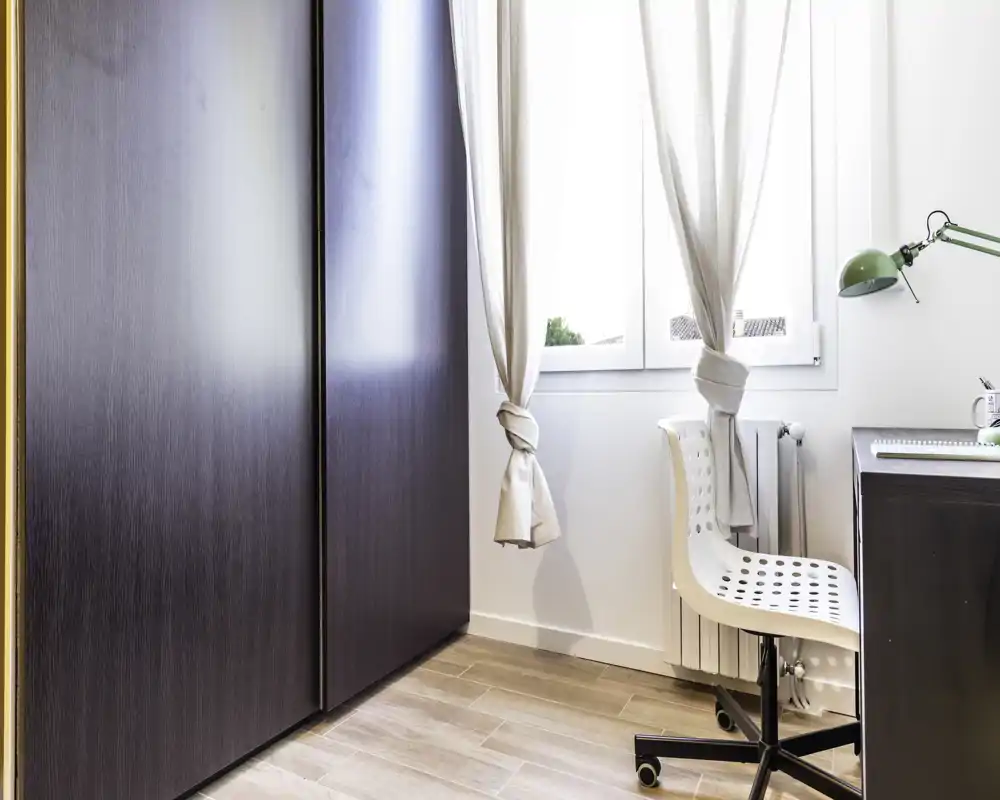 Coin lumineux et minimaliste avec armoire, fenêtre et petite chaise de bureau — un espace de vie/étude compact baigné de lumière naturelle.