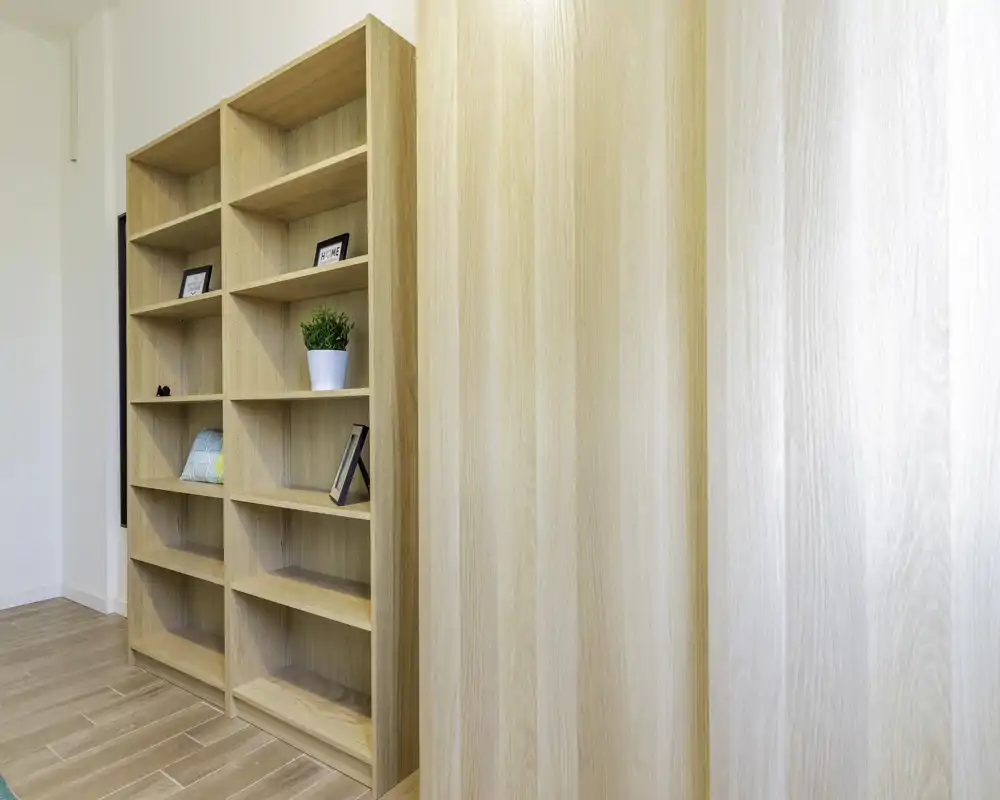 Stanza luminosa e minimalista con alti scaffali in legno e pavimento in legno chiaro — area living neutra o angolo relax ideale per esporre libri e oggetti decorativi.