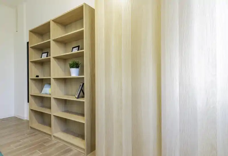 Bright, minimalist room with tall wooden shelving and light wood flooring — a neutral living area or lounge corner ideal for displaying books and decorative objects.