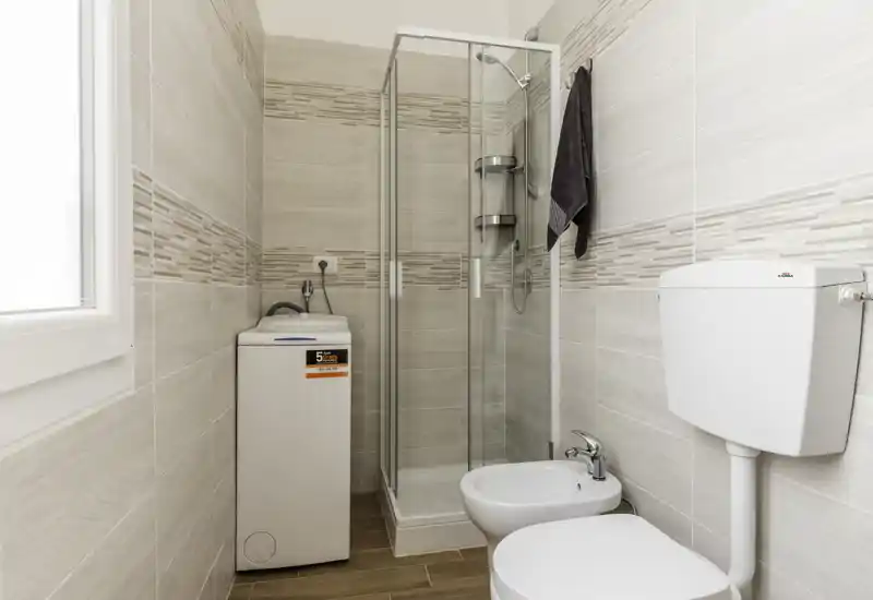 Bright, modern bathroom with a glass shower enclosure, bidet and toilet; light neutral tiles and wood-effect floor create a clean, contemporary look.