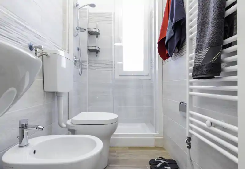 Bright, modern bathroom with a shower stall, toilet and bidet; light gray tiles and a heated towel rail create a clean, contemporary feel.