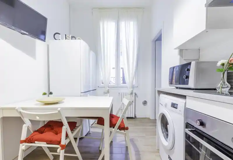 Bright, compact kitchen with a dining table, modern appliances and cozy red chair cushions—ideal for a small city apartment.
