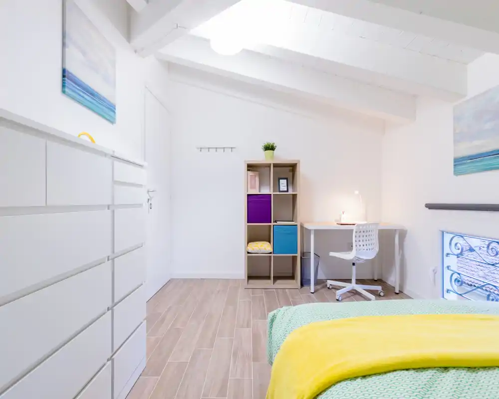 Dormitorio moderno y luminoso con la cama bien hecha en primer plano, un escritorio compacto y estantería contra la pared, decoración de estilo nórdico.