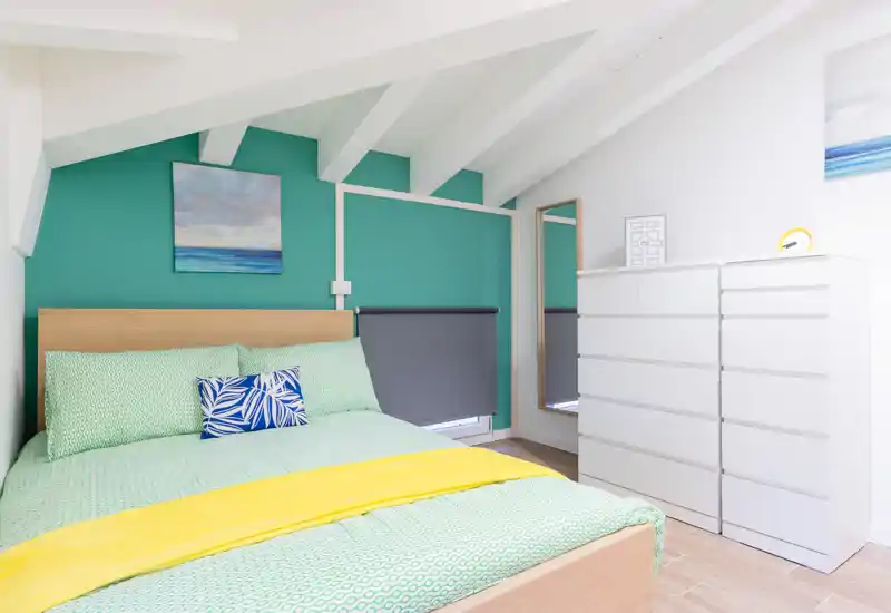 Dormitorio luminoso y cuidado con cama doble, ropa de cama estampada y una cómoda blanca bajo techo inclinado: una habitación ático moderna y acogedora.