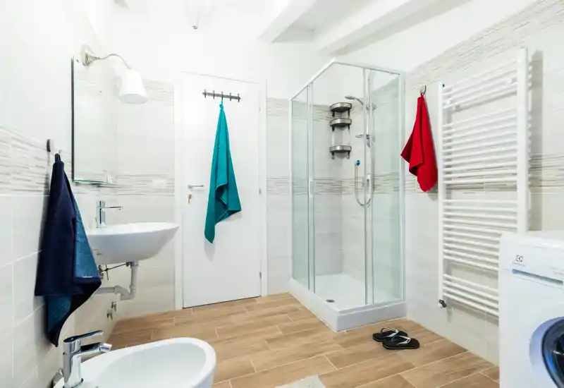 Modern, bright bathroom with walk-in shower, wall-mounted sink and tiled wood-effect floor; white fixtures and colorful towels add refreshing contrast.