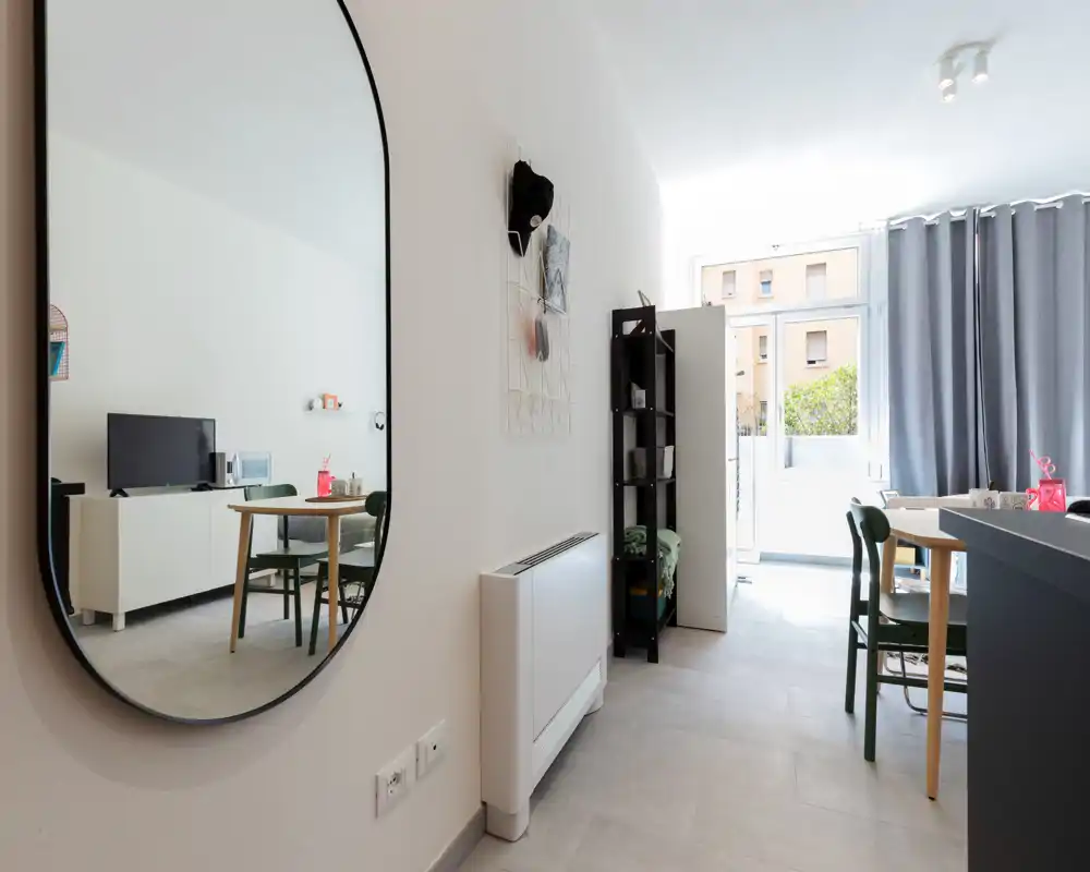 Bright, modern living area with a dining table, chairs and a TV cabinet; large mirror and natural light create an airy, welcoming space.