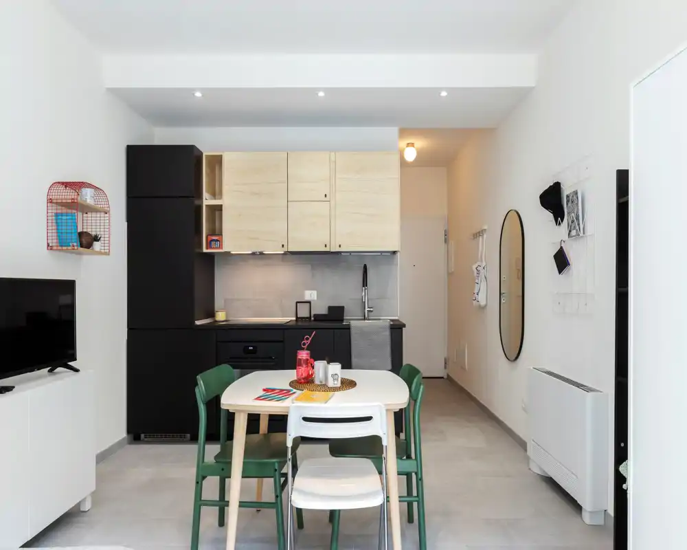 Bright, modern open-plan kitchen with a small dining table and four chairs, light wood cabinets and matte black lower units creating a clean, contemporary look.
