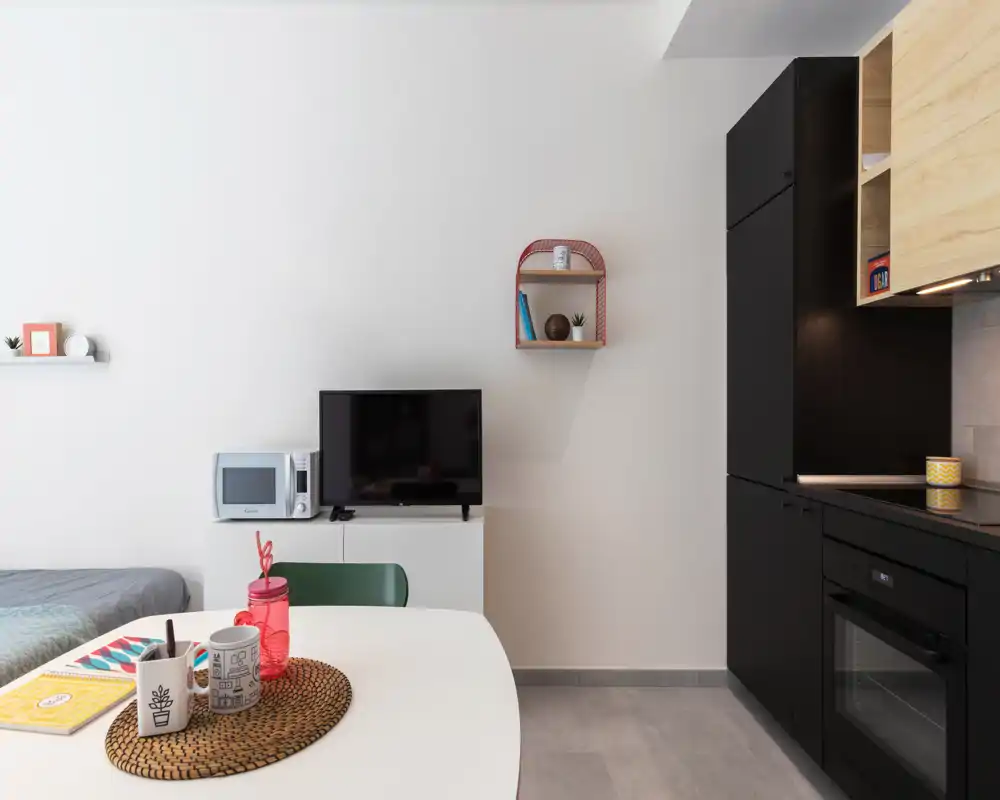 Compact studio living area with a small dining table, TV console and kitchenette. Clean modern styling with simple decorative touches makes it suitable for short-term rentals.