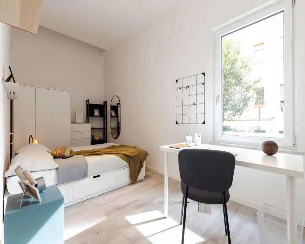 Dormitorio moderno y luminoso con cama individual, cajones bajo la cama y escritorio junto a la ventana. Líneas limpias, luz natural y decoración minimalista, ideal para estudiantes o profesionales.
