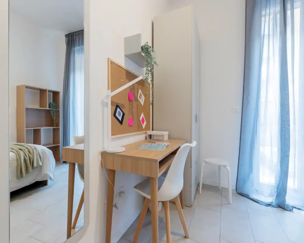 Rincón de dormitorio moderno y luminoso con escritorio de madera y cama visible en un espacio aireado y bien iluminado — ideal para una estancia cómoda o para trabajar desde casa.