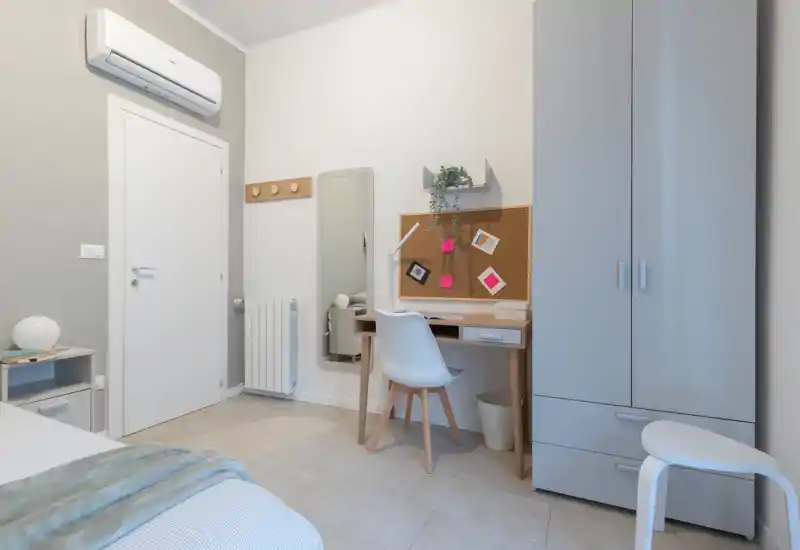 Rincón de dormitorio luminoso y moderno con cama individual ordenada, escritorio compacto y armario — ideal para estudiante o una sola persona.