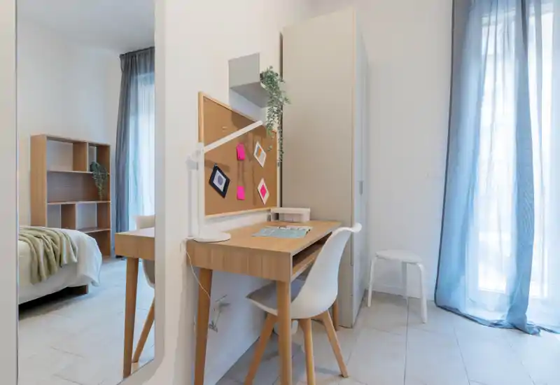 Rincón de dormitorio moderno y luminoso con escritorio de madera y cama visible en un espacio aireado y bien iluminado — ideal para una estancia cómoda o para trabajar desde casa.