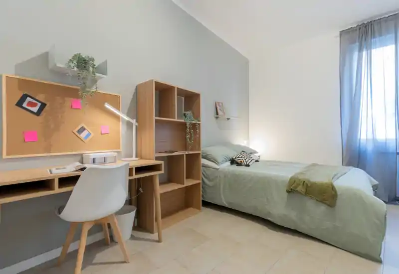 Camera singola ben arredata con letto ordinato, tessili accoglienti e una scrivania funzionale vicino alla finestra — luminosa, moderna e tranquilla.