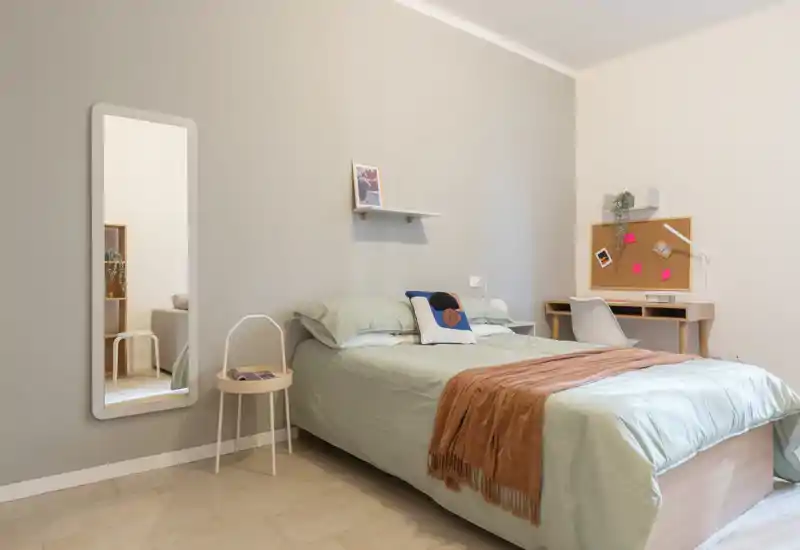 Camera da letto luminosa e minimal con letto matrimoniale ordinato, biancheria verde tenue, un plaid caldo e una piccola postazione di lavoro nell'angolo — perfetta per soggiorni tranquilli.