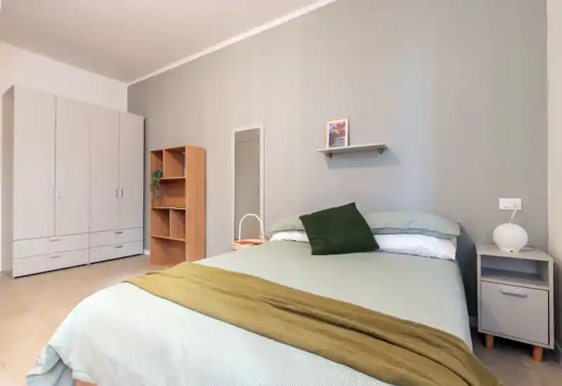 Dormitorio luminoso y ordenado con cama doble, mesita y armario; textiles verdes y decoración sencilla que crean un ambiente tranquilo y acogedor.