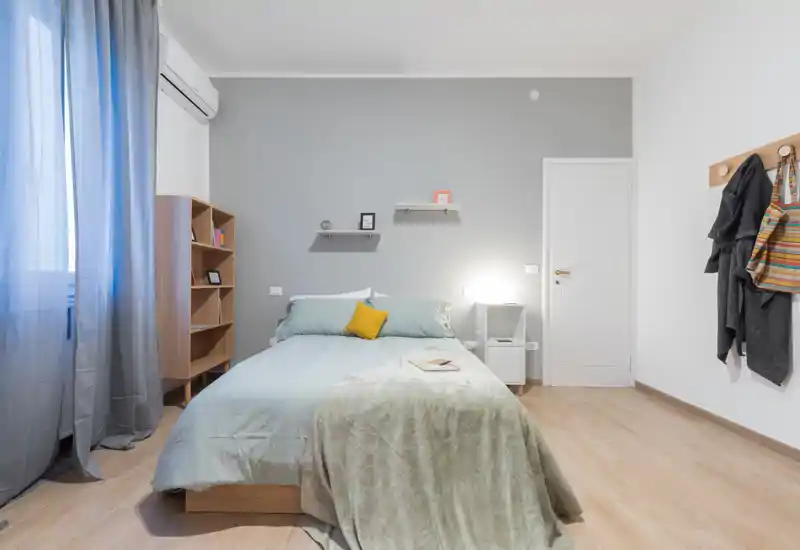 Camera da letto moderna e luminosa con letto matrimoniale centrale, biancheria morbida, comodino e mensole semplici — stile accogliente e luce naturale.