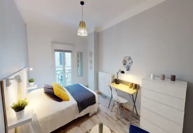 Camera da letto moderna e luminosa con letto matrimoniale ben rifatto, cuscini decorativi, lampada da comodino e una piccola scrivania vicino alla finestra — perfetta per un soggiorno confortevole o smart working.