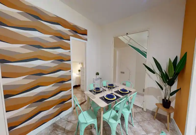 Zona pranzo luminosa e curata con tavolo apparecchiato per sei, sedie in metallo verde menta e parete decorativa dai toni caldi—ideale per mostrare l'area pranzo dell'appartamento.