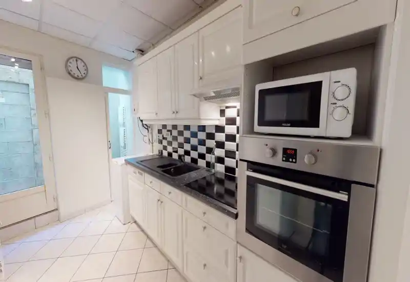 Cucina luminosa e ordinata con mobili bianchi, paraschizzi a tasselli bianco-nero, forno e microonde incassati e piano cottura a induzione. Ripiani puliti e disposizione efficiente per cucinare.