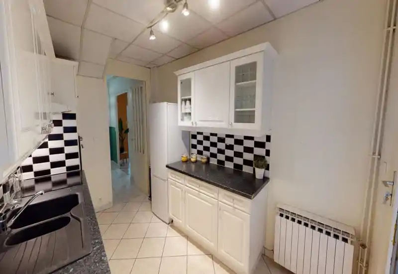 Cucina compatta e luminosa con pensili bianchi, piano di lavoro nero e paraschizzi a piastrelle bianche e nere; presenta lavello, frigorifero e vetrine superiori — spazio pulito e funzionale adatto a un annuncio.