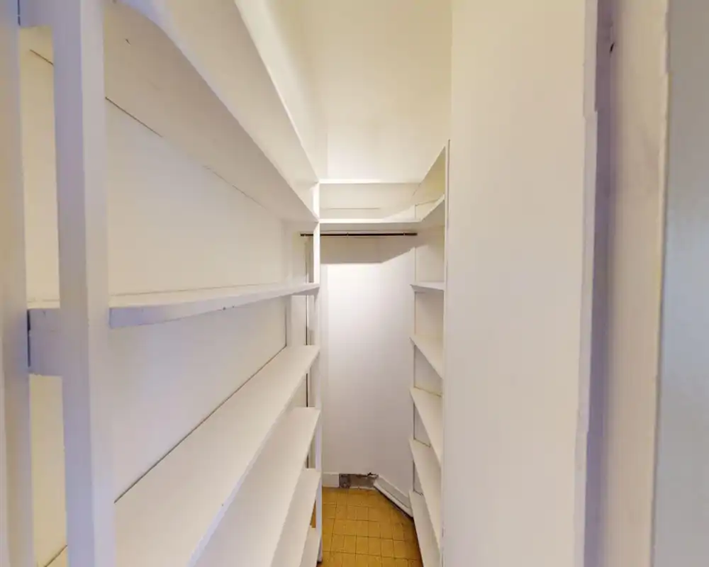 Narrow built-in storage/closet with multiple white shelves and a small floor area — ideal for pantry or linen storage.