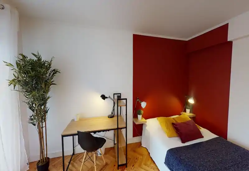 Bright, stylish bedroom with a deep red accent wall, comfortable bed with colorful cushions and bedside lamps, plus a practical desk and chair for work or study.