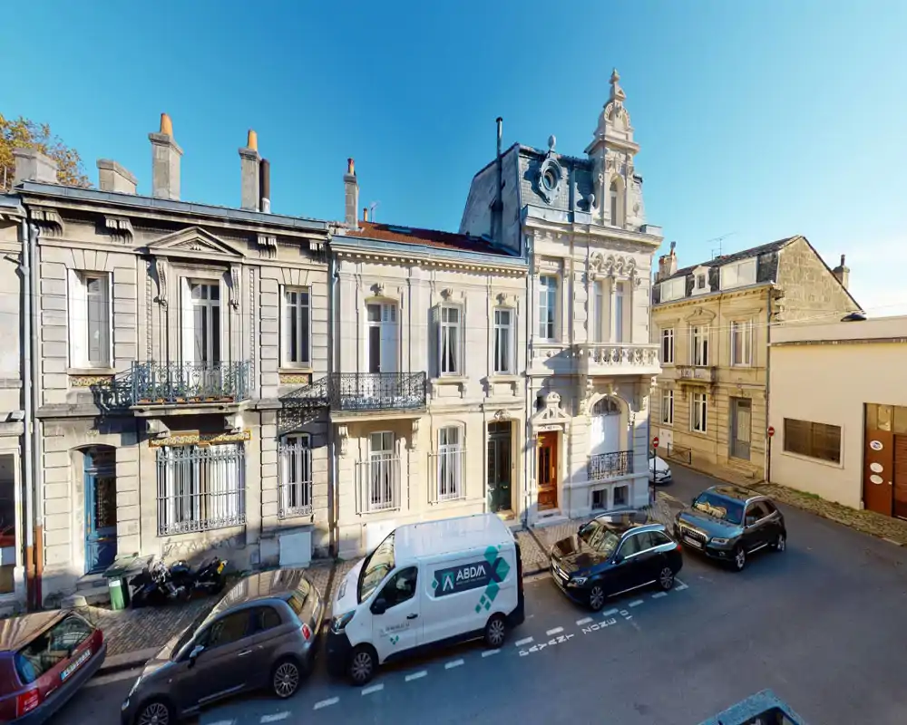 Immagine luminosa a livello strada di una facciata storica e decorata con auto parcheggiate e cielo blu, ideale per mostrare l'esterno e il contesto stradale.
