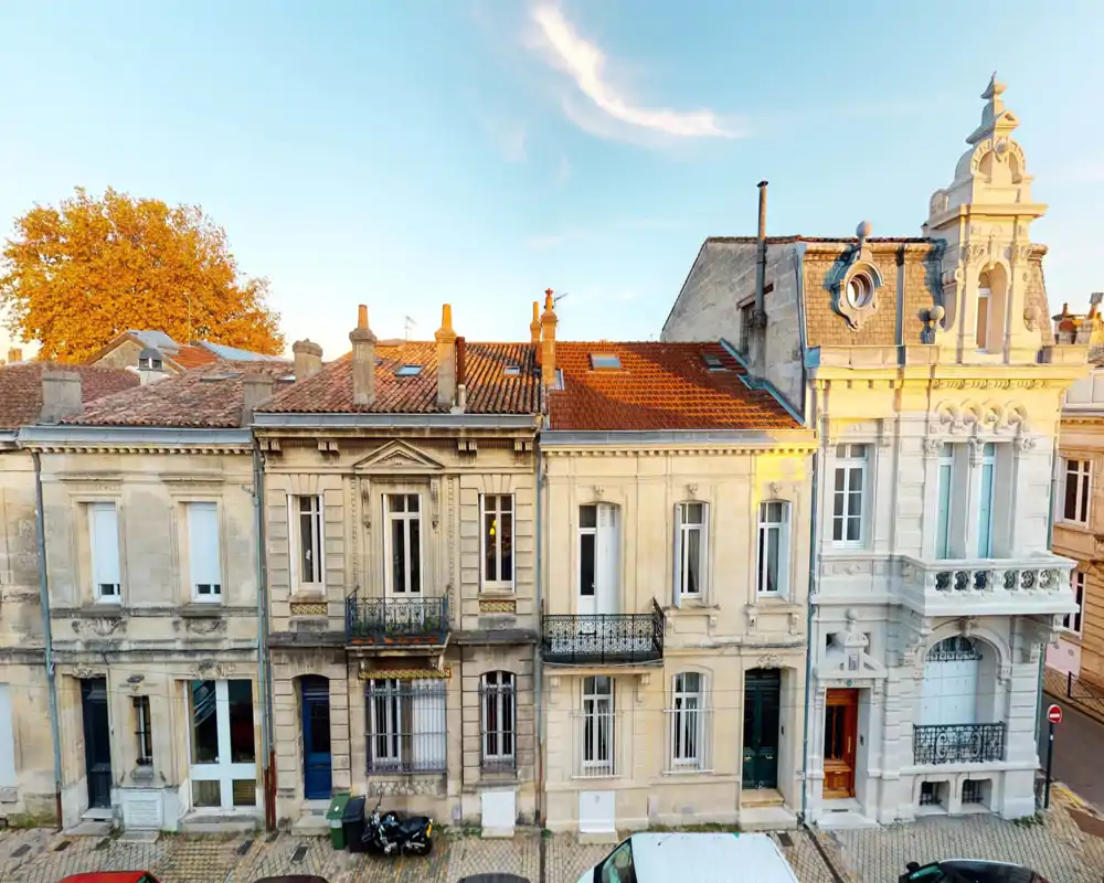 Vue extérieure d'une rangée de maisons de ville en pierre à l'heure dorée : façades ornées, balcons et toits en tuiles visibles depuis la rue.