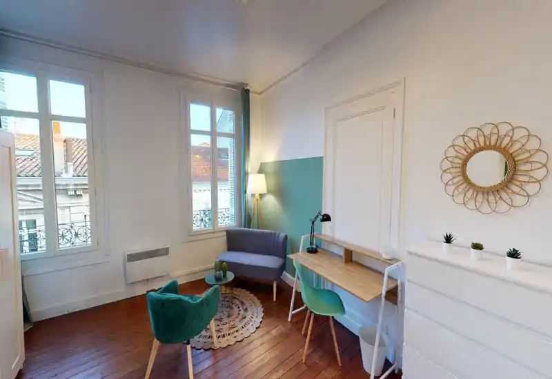 Espace de vie lumineux et élégant avec un petit canapé, un fauteuil, un bureau et de grandes fenêtres apportant une belle lumière naturelle — idéal pour se détendre ou télétravailler.