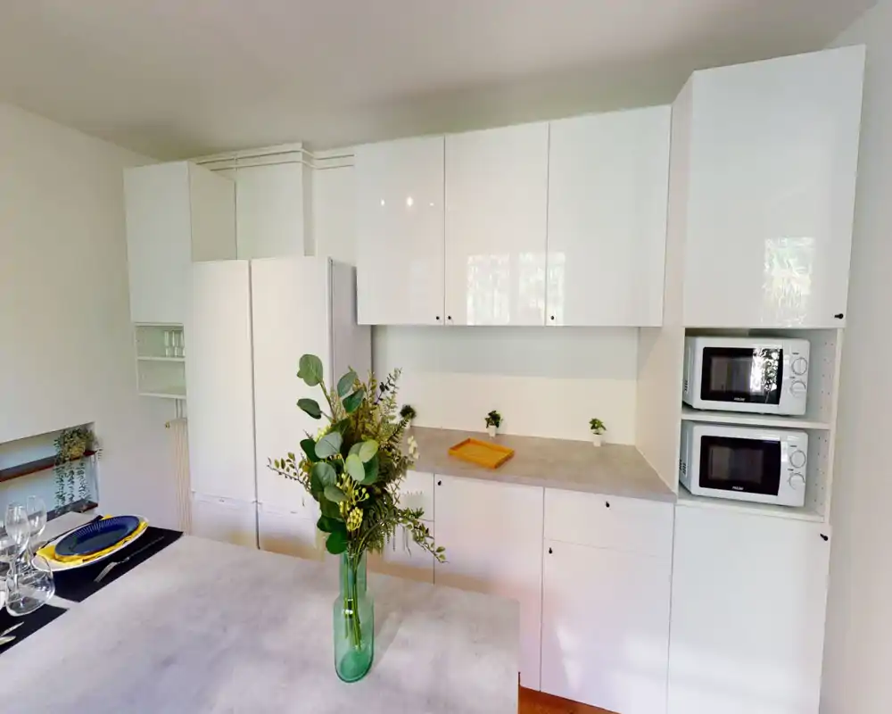 Cuisine moderne et lumineuse avec placards blancs, électroménagers intégrés et un plan central décoré d’un vase de verdure — un espace de préparation propre et bien éclairé.